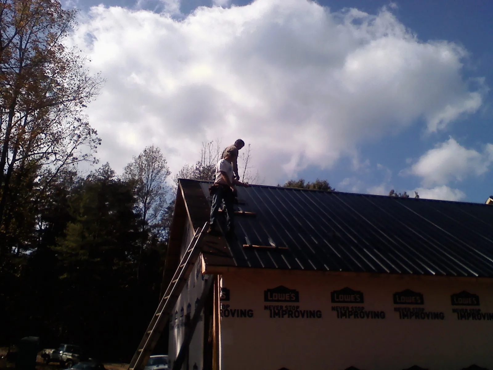 Roofer fastening dark metal panels high against a cloudy sky in New Market